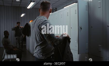 Three Diverse Industrial Workers in High Visibility Gear Friendly Interact, Laugh, and Share Jokes While Dressing For Their Shift in Modern Factory Facility. Corporate Culture and Team Spirit. Stock Photo