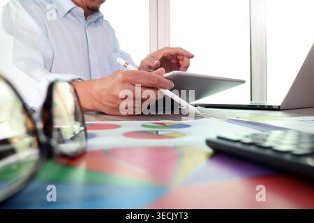 Business professional using digital tablet and stylus at office desk with laptop, calculator, financial charts, and documents for analysis and plannin Stock Photo