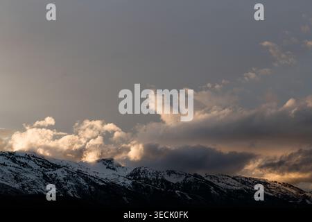 Storm clouds gathering over snowy mountain range at dusk Stock Photo