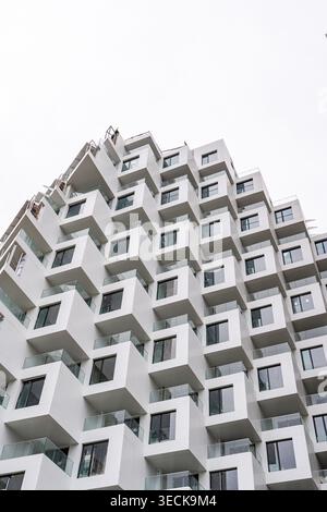 Low angle view of a modern high-rise with curved concrete and metal structure, featuring repeating cube balconies and large glass windows against a cl Stock Photo