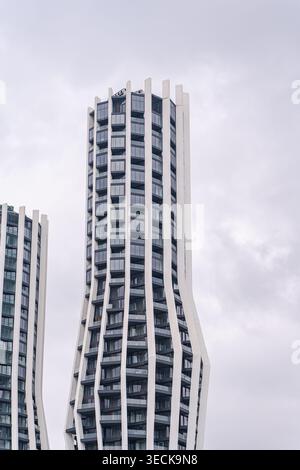 Modern high-rise tower with a curving facade, combining concrete fins, reflective glass panels, and metal framing against a soft cloudy sky, showcasin Stock Photo