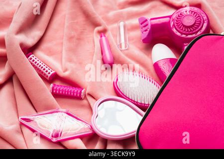 Pink pretend play hairdresser kit on soft fabric with toy dryer, brush, mirror and cosmetic props, creating a cute girlhood beauty salon scene in a pi Stock Photo