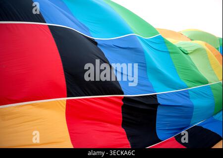 Close up of colorful hot air balloon fabric with bold striped panels, lying on the ground during inflation before flight, showing texture, seams, and Stock Photo