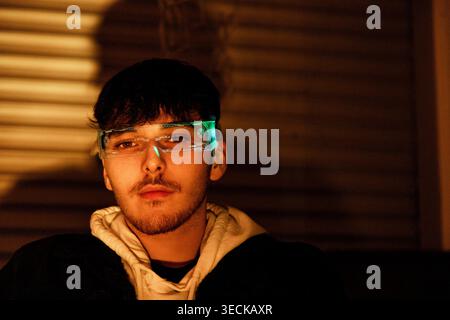 Close up portrait of a young man wearing futuristic cyber glasses with neon interface at night, warm cinematic lighting and moody shadows, technology Stock Photo