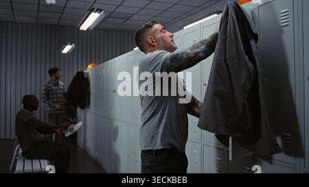 Three Diverse Industrial Workers in High Visibility Gear Friendly Interact, Laugh, and Share Jokes While Dressing For Their Shift in Modern Factory Facility. Corporate Culture and Team Spirit. Stock Photo