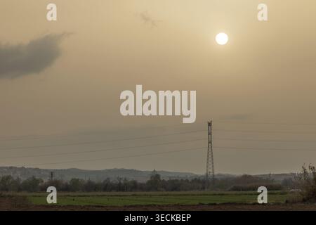 Power lines stretch across an open landscape at sunset, highlighting the essential energy infrastructure as the soft golden hues of twilight create a Stock Photo