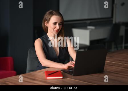 Focused businesswoman works on a laptop at a modern office desk with notebook and pen, planning tasks and managing projects in a calm professional wor Stock Photo
