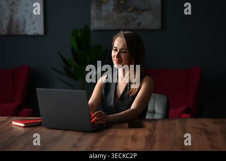 Confident business woman working on a laptop at a wooden desk in a modern office, planning tasks and communicating online, with soft light, copy space Stock Photo