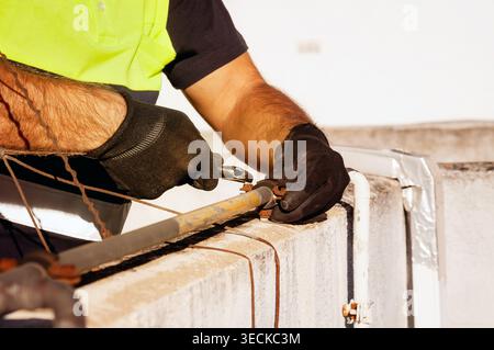 Close up of an industrial maintenance technician wearing safety glove and high visibility vest using plier to repair a metal pipe on a concrete unit, Stock Photo