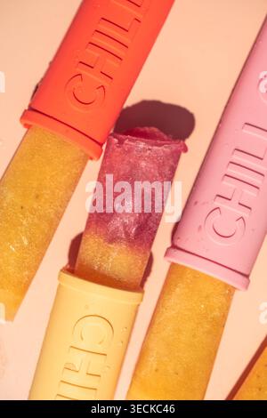 Close-up of homemade fruit ice popsicles in colorful reusable molds, showing vibrant layers and frosty texture on a pastel background, perfect for sum Stock Photo