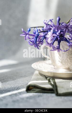 A close-up of a beautiful purple hyacinth elegantly placed in a textured white teacup, set on a neatly folded cloth, exuding a serene springtime ambia Stock Photo