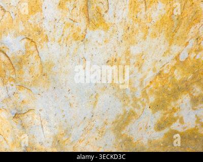Close-up of weathered stone surface with warm ochre stains and pale mineral speckles, creating an abstract natural pattern texture for background desi Stock Photo