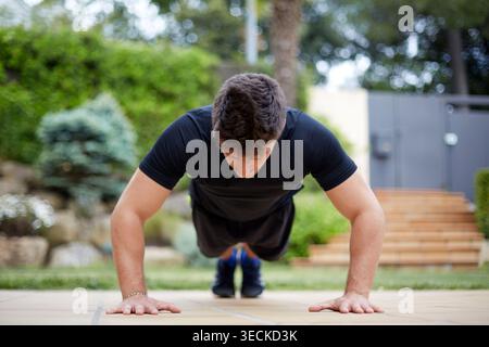Athletic man doing push ups on a paved patio in a garden, focused on strength training, bodyweight exercise, and healthy active lifestyle outdoors. Stock Photo
