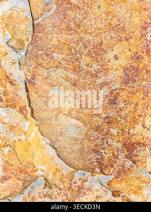 Close-up of weathered stone surface with rusty orange and beige mineral tones, natural crack lines, and mottled abstract texture ideal for background Stock Photo