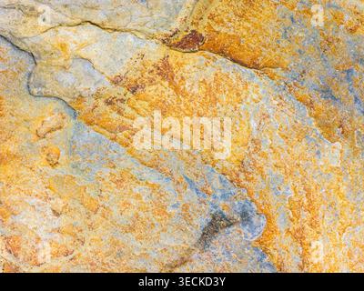 Close-up abstract stone surface with layered cracks and weathered mineral stains in rust, ochre, and soft blue tones, forming a natural pattern backgr Stock Photo