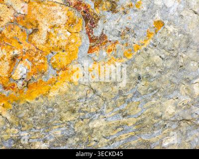 Close-up of weathered stone surface showing abstract natural patterns, with gray and beige layers, rusty orange mineral stains, and rough cracked text Stock Photo
