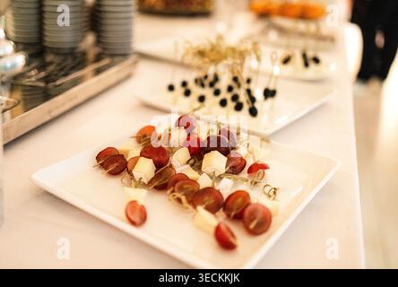 Assorted appetizers with skewered grapes and cheese cubes displayed on white plates, with additional food items visible in the background at a caterin Stock Photo