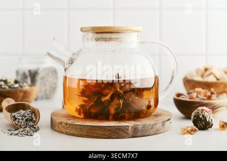 Blooming tea in a glass teapot with dry tea leaves, brown sugar in bowls, and ingredients on a light background. Concept of tea ceremony, natural beve Stock Photo