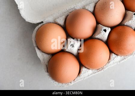Top view of brown raw eggs in a cardboard carton on a light background. Concept of natural food, farming, and minimal kitchen ingredients. Stock Photo