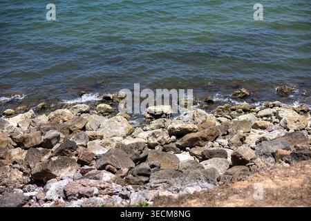 Peaceful rock shore by calm ocean water forming beautiful coastal shoreline scene with gentle waves washing against stone barrier in serene nature lan Stock Photo