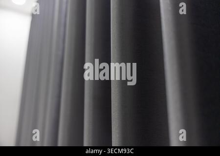 Close up dark fabric curtain drape displaying smooth vertical fold texture in elegant grey tones creating mysterious calm mood for abstract background Stock Photo