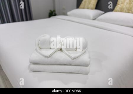 White heart shaped towels placed on clean bed in hotel room ready to welcome guests with warm hospitality, creating romantic and peaceful atmosphere f Stock Photo