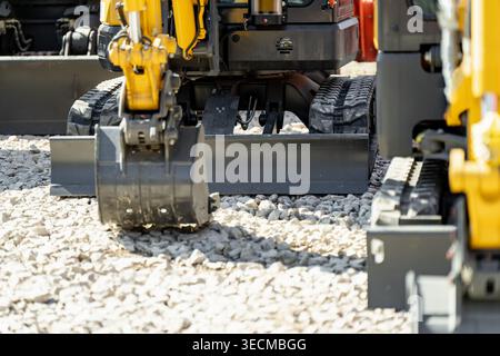 Mini excavator with black metal bucket and dozer blade resting on light grey gravel stones at a construction site, representing compact engineering an Stock Photo
