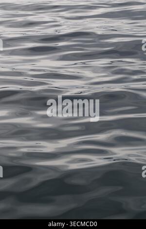 Textured vertical view of dark gray and blue wavy sea surface with gentle ripples. Stock Photo