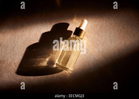 Glass dropper bottle containing golden serum rests on a textured surface, with soft lighting creating a shadow and highlighting the product's design Stock Photo