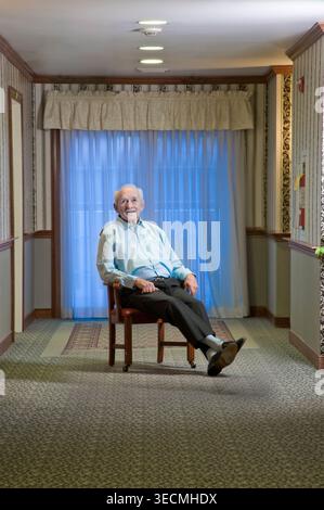 Older man sitting in chair in hallway smiling, Philadelphia USA Stock Photo