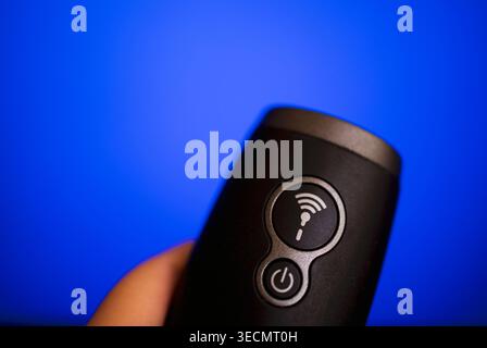 Close-up view of a black remote control featuring Wi-Fi and power buttons, held in a hand with a blue background highlighting modern technology Stock Photo