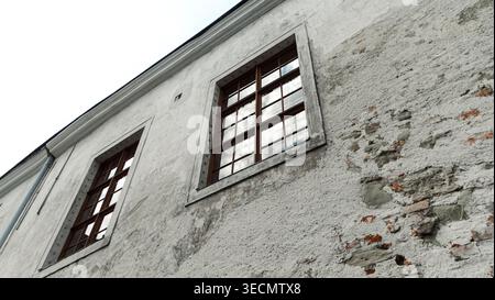 Old weathered building facade with peeling plaster reveals patches of exposed brick, suitable for design and background use.  Stock Photo