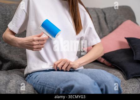 Woman in white t-shirt uses reusable washable adhesive lint roller with blue gel to clean white t-shirt at home. Concept of sustainable clothing care Stock Photo