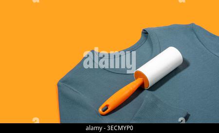 Sticky adhesive lint roller with for removing pet hair on teal top on bright orange background. Concept of quick clothing cleaning, everyday household Stock Photo