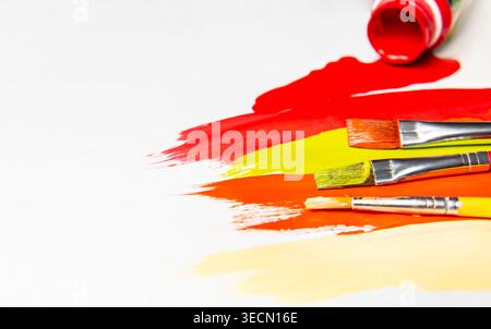 Several paintbrushes rest on colorful paint strokes on a white surface with paint tubes positioned at the top. Stock Photo