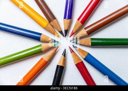 Pencils of different colors are placed in a circular pattern on a white surface with sharp tips pointing inward. Stock Photo