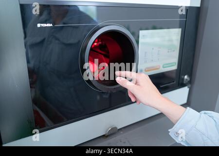 Hand next to circular opening on modern recycling machine. Red light glows. User interacts with sleek, digital interface. Stockholm, Sweden, 18 May 20 Stock Photo