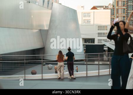 Couple standing on balcony looking at modern urban architecture in city space, Man and woman enjoying view in contemporary plaza with cityscape and Stock Photo