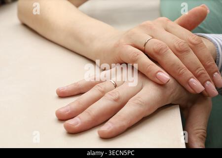 Two hands rest gently atop each other. Fingernails polished, clean, and short. Rings sit modestly on each ring finger. Soft skin tone and natural nail Stock Photo