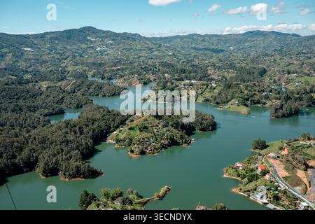 Guatapé reservoir showcasing emerald green waters surrounded by green mountains, small islands, and scattered houses under a blue sky, reflecting the Stock Photo