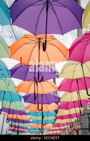 Bright colorful umbrellas suspended overhead form a playful canopy along a city street, creating vibrant shade and eye-catching street art for a sunny Stock Photo