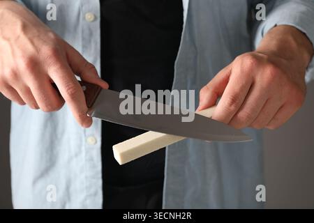 Man sharpening knife on grey background, closeup Stock Photo