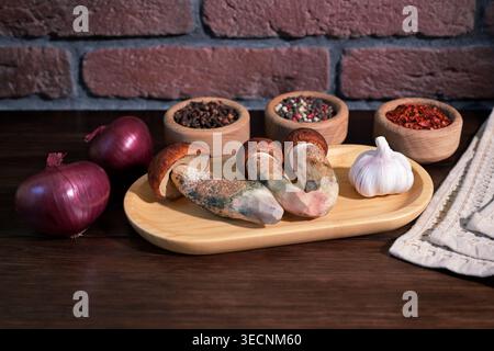 Wild mushrooms Leccinum aurantiacum on wooden plate with garlic, red onions and spices on rustic table Stock Photo