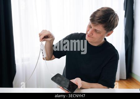 Man holding smartphone and connecting it to white USB hub adapter with multiple ports, managing connections for various electronic devices on white Stock Photo