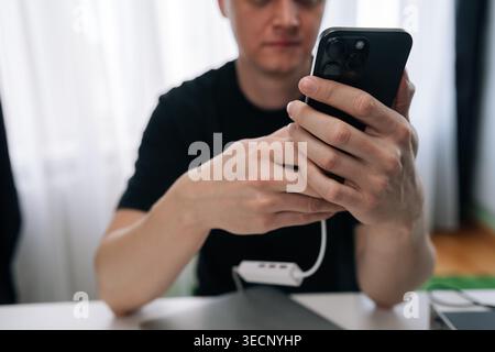 Man holding and charging smartphone, connecting it to multi port adapter with white cable, concept of modern technology use and constant connectivity Stock Photo