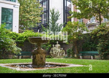 A serene urban courtyard garden featuring a central stone fountain with water gently flowing into a square basin filled with smooth stones. The Stock Photo