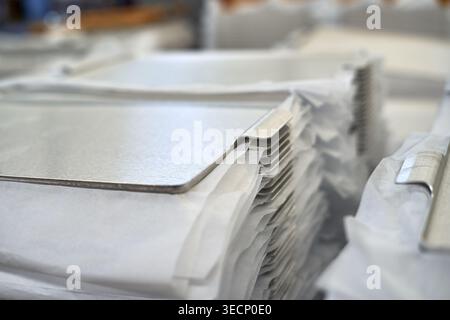Close-up view of stacked flat metal sheets separated by white protective paper in an industrial warehouse or manufacturing facility. The metallic Stock Photo