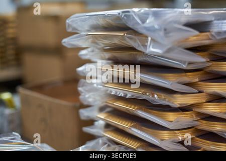 A close-up view of multiple stacks of golden-colored packaged goods sealed in clear transparent plastic bags, arranged in neat horizontal piles. The Stock Photo
