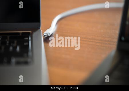USB C Cable Connected to Laptop on Wooden Desk Stock Photo