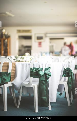 Elegant wedding reception setup with white chairs adorned with green satin bows and table settings Stock Photo